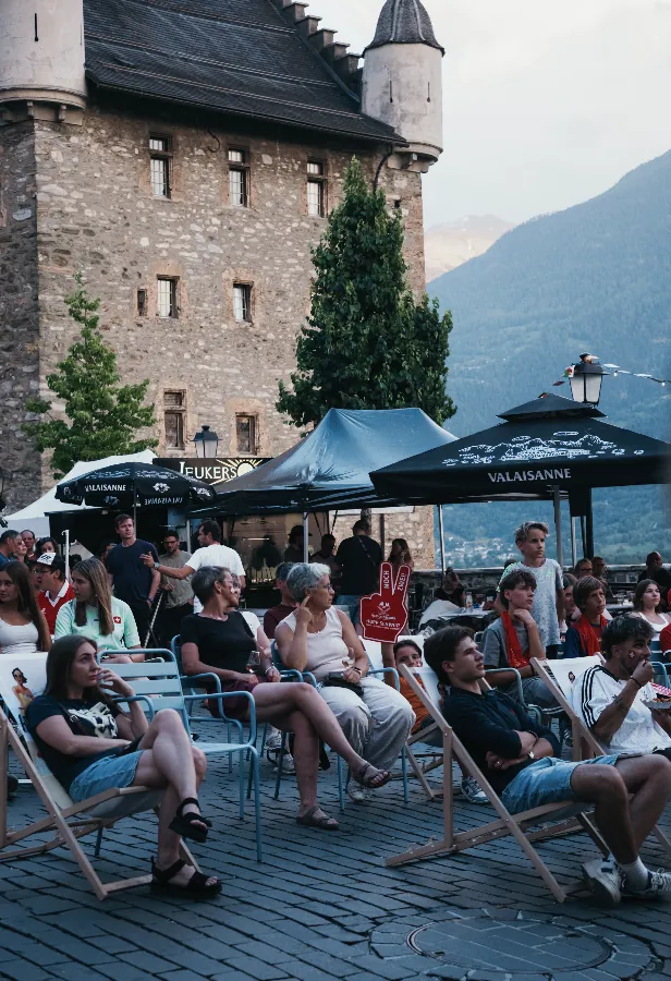 Gäste sitzen am Abend unter Sonnenschirmen vor dem Turm der Burg Leuk